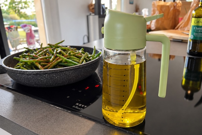 Pschit à huile gradué posé à côté d'une poêle de haricots verts